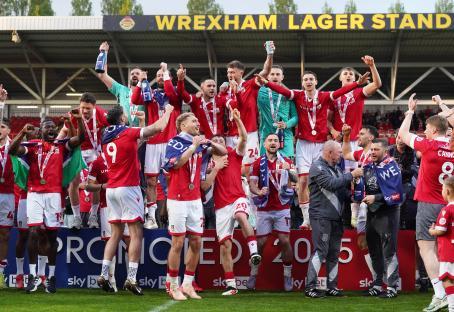 Wrexham AFC players celebrating promotion, holding trophy and medals.