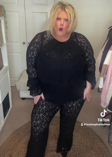 A plus-size woman models a black lace top and pants for a Christmas/party outfit.
