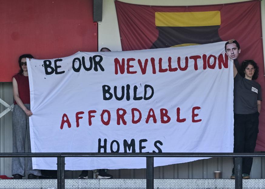 Fans holding a banner that reads "Be our Nevillution Build Affordable Homes."
