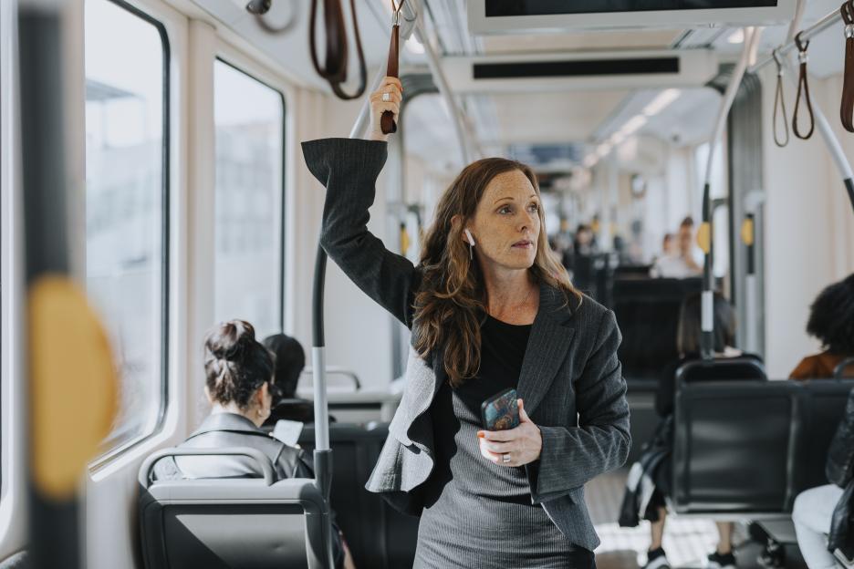 Female commuter holding smartphone while standing in train.