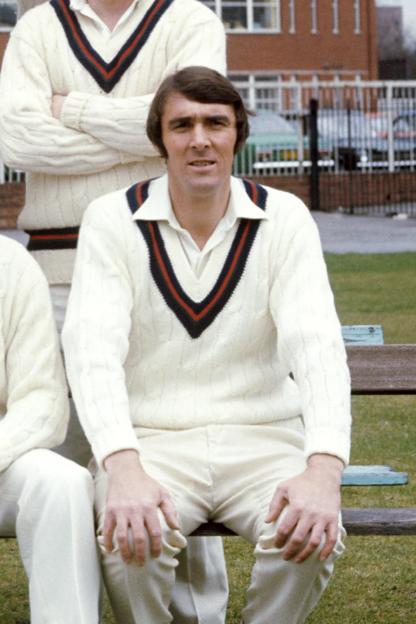 Photo of a cricketer in whites sitting on a bench.