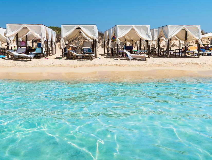 A sandy beach with white canopy tents and turquoise water, Pescoluse, Italy.