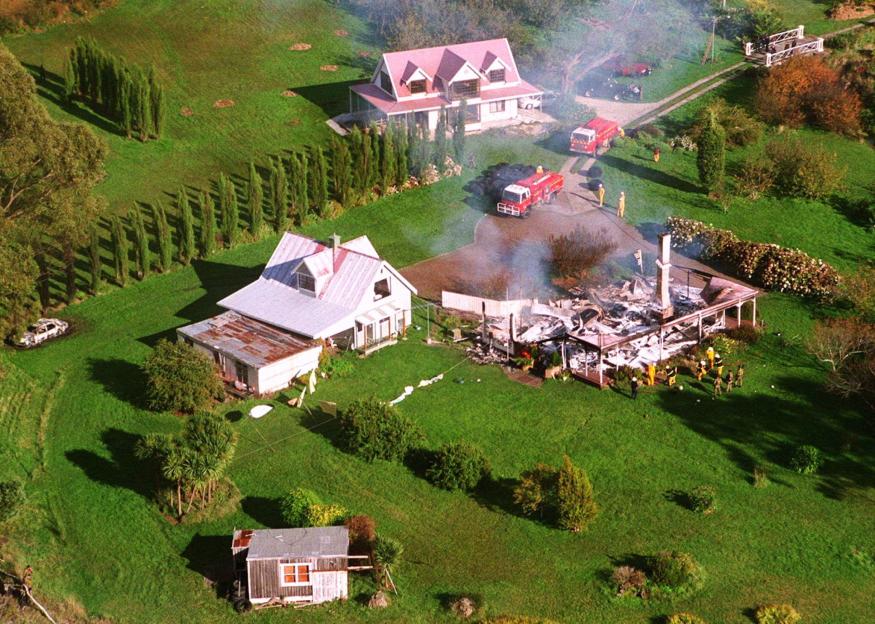 Aerial view of a burnt guesthouse with fire trucks and emergency personnel, with another house nearby.