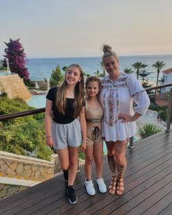 Woman and her two daughters posing on a balcony overlooking the ocean.