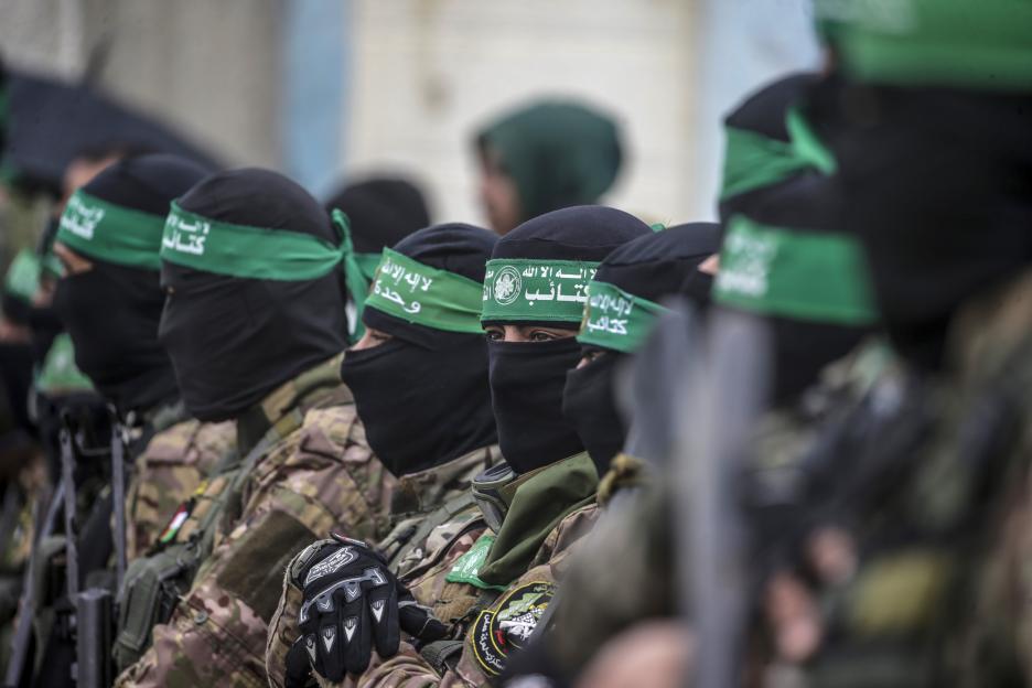 Armed Hamas fighters in camouflage uniforms and black balaclavas, one with a green headband, stand guard.