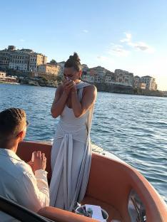 A woman cries happily as a man proposes on a boat.