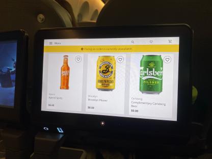 Airplane in-flight entertainment screen showing beverage options: Aperol Spritz ($6.50), Brooklyn Pilsner ($8.50), and complimentary Carlsberg beer.