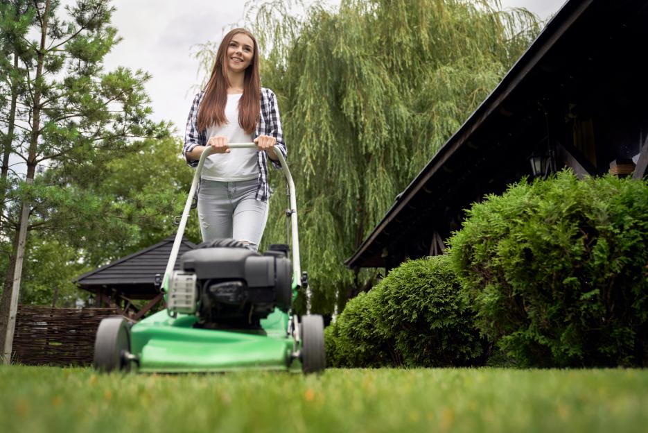 Woman mowing lawn with a green lawnmower.