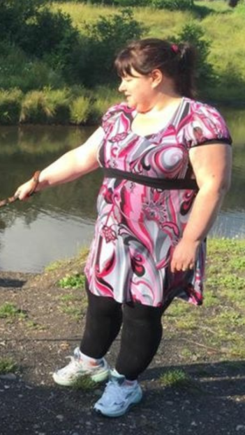 Woman in patterned dress walking a dog by a pond.