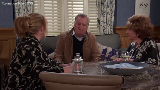 Screenshot from Coronation Street showing three characters seated at a table.