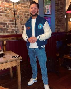 Man in varsity jacket standing in a pub.