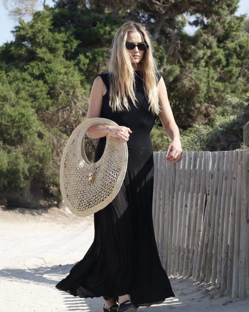 Margot Robbie walking in Ibiza, carrying a large, round straw bag.