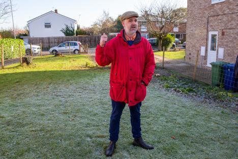 A man in a red jacket stands in a frosty yard, gesturing.