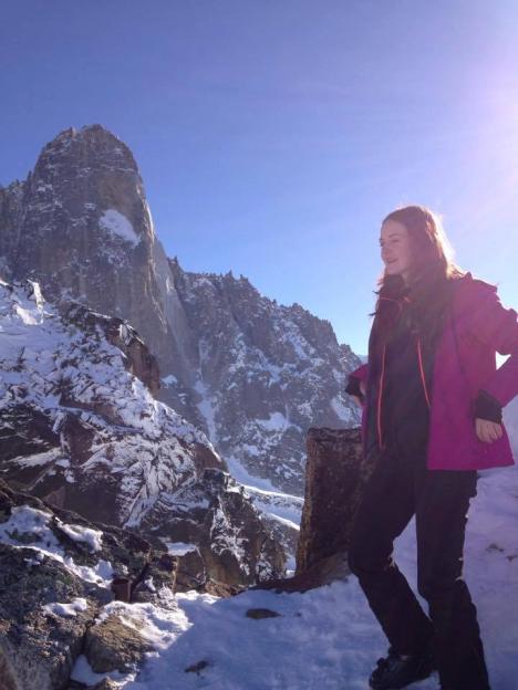 Woman in pink jacket standing on snowy mountain peak.