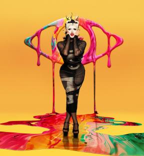Danny Beard in a black dress, standing in front of a large, colorful eye illustration.