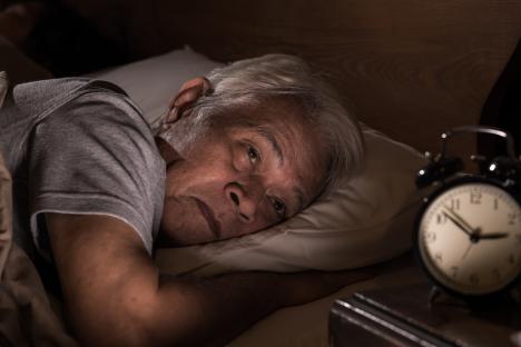 Depressed senior man lying in bed unable to sleep.
