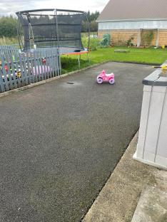 Driveway with a pink toy car and trampoline in the background.