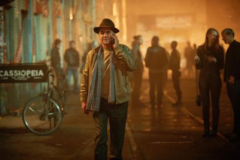 Man in hat talking on cell phone on a city street at night.