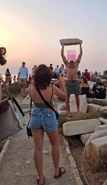 Tourist lifting ancient stone block at sunset.