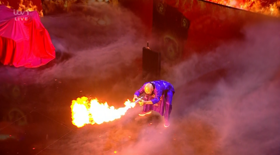 A performer breathes fire on a stage.