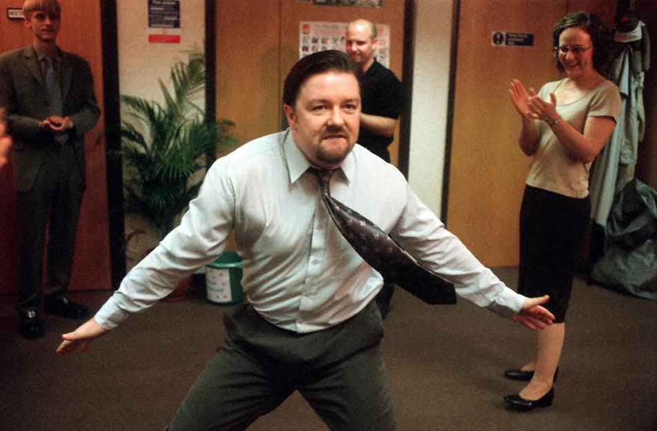 David Brent from The Office dancing awkwardly for his colleagues, Tim, Gareth, and Dawn, who are watching.