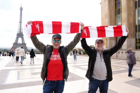 Two Arsenal fans in Paris holding up a team scarf in front of the Eiffel Tower.