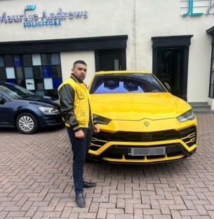 Man in yellow jacket standing next to yellow Lamborghini.