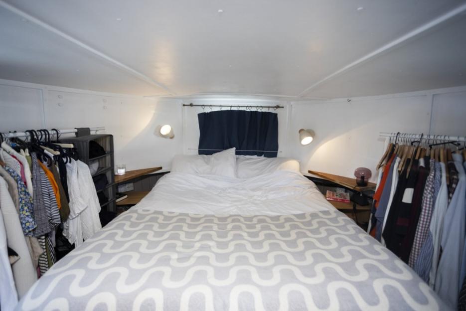 Bedroom on a houseboat with a bed and clothes hanging on racks.