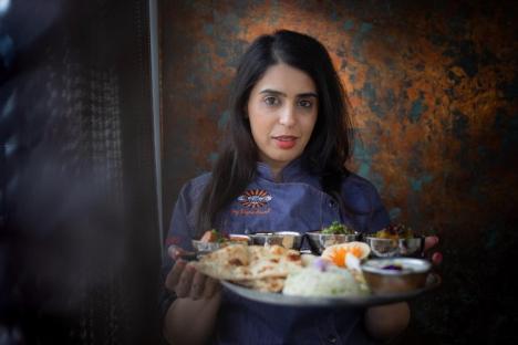 A woman chef holding a platter of Indian food.