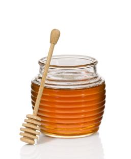 A glass jar of honey with a wooden honey dipper.