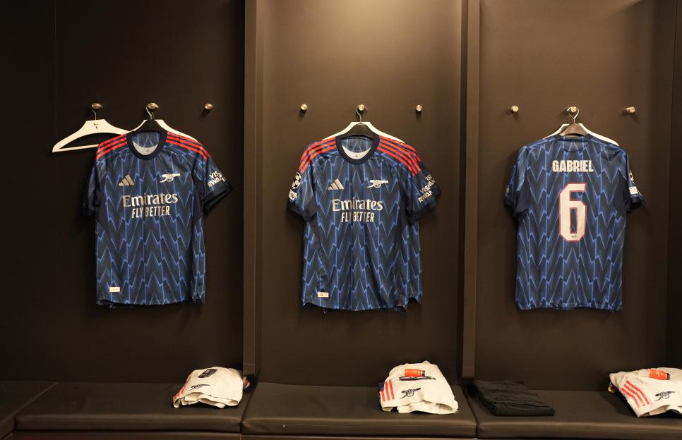 Three Arsenal shirts hanging in a locker room.