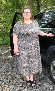 Woman in leopard print dress standing by car.