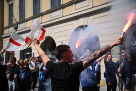 A man with a tattooed arm holding a lit flare, surrounded by other people holding flags and flares.