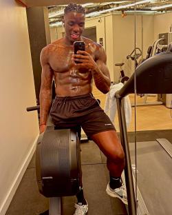 Shirtless man taking a selfie in a gym.