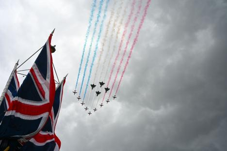 Military jets fly in formation over Union Jack flags during a VE Day parade.