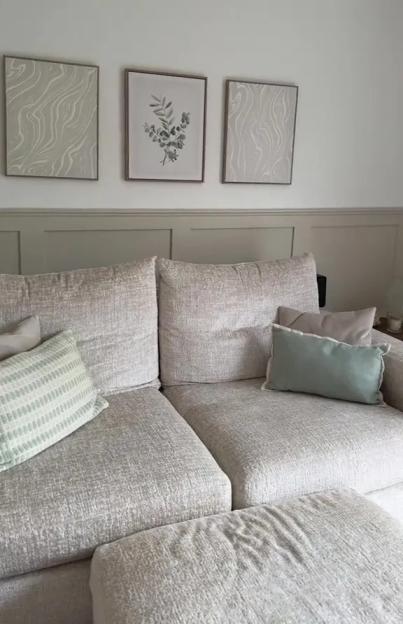 A light-colored sofa with throw pillows in a room with framed art and decorative wall molding.