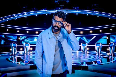 Man in glasses on game show set.