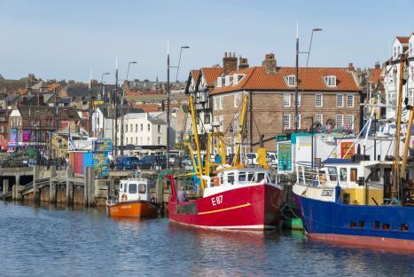 Colourful scene around the harbour in the historic seaside town of Scarborough on the east coast of England. Popular with holidays makers and daytrippers the town has many attractions. Traditional fishing boats moored beside the seafood stalls. Sept 2016.