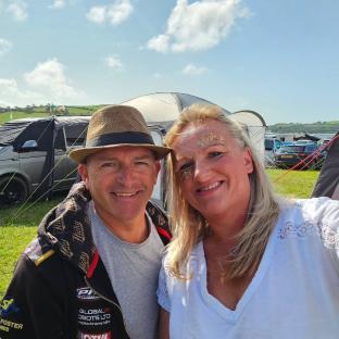 A couple smiling for a selfie at a campsite.
