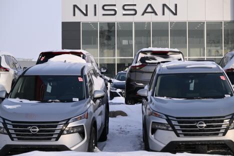 Snow-covered Nissan cars parked at a dealership.