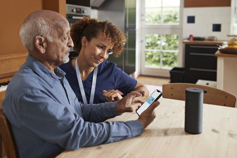 A female nurse assisting a senior man in booking an online appointment through a smartphone.
