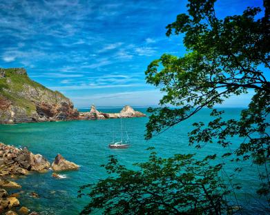 Sailboat in a cove near rocky cliffs.