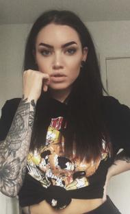 Woman with tattoos and dark hair wearing a band t-shirt.