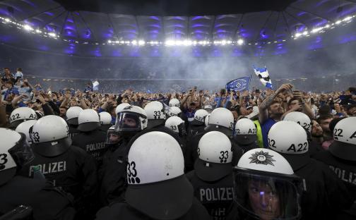 Police officers in riot gear face celebrating soccer fans.
