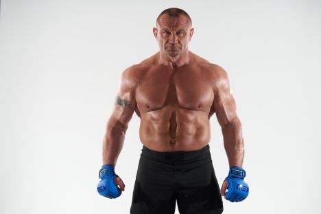 Portrait of a muscular man wearing blue KSW gloves.