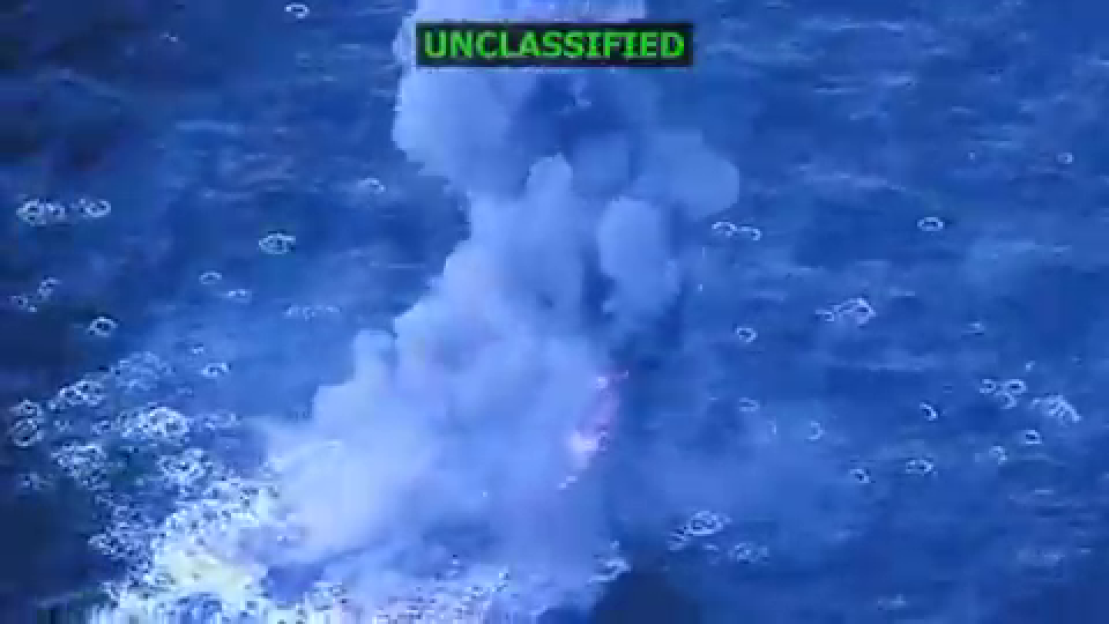 An explosion in dark blue water, with a small green box in the upper right that says "UNCLASSIFIED."