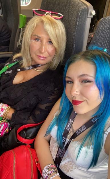 Photo of a mother and daughter on a train, both wearing Taylor Swift Eras Tour lanyards.