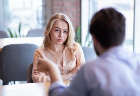 A young woman sits with her arms crossed, looking unhappy during a date at a cafe.