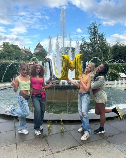 Four women posing with a 1M balloon in front of a fountain.