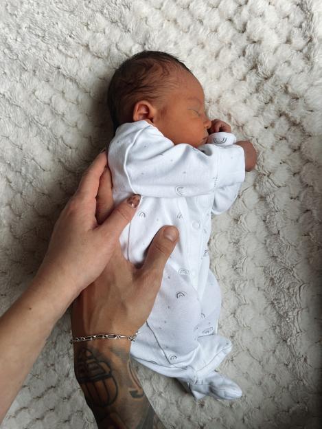 A parent's hands gently cradling their sleeping newborn on a soft white blanket.